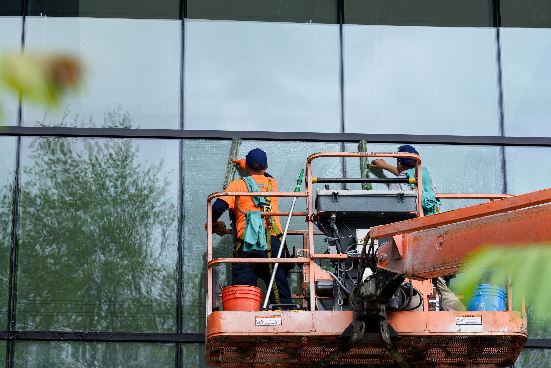 A window cleaner in a high-visibility shirt soaping a glass panel from a lift platform