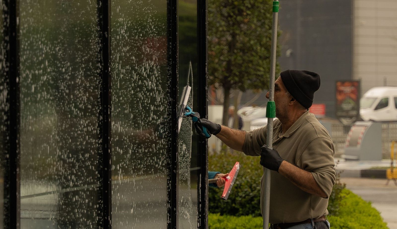 A window cleaner working a wall of storefront glass with a pole and squeegee